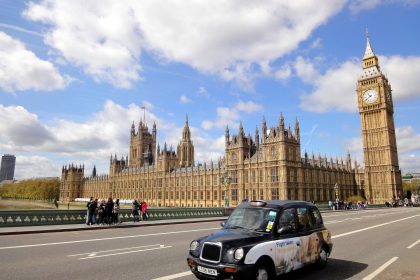 london black cab on the road in front of the houses of parliament with a blue sky and white clouds
